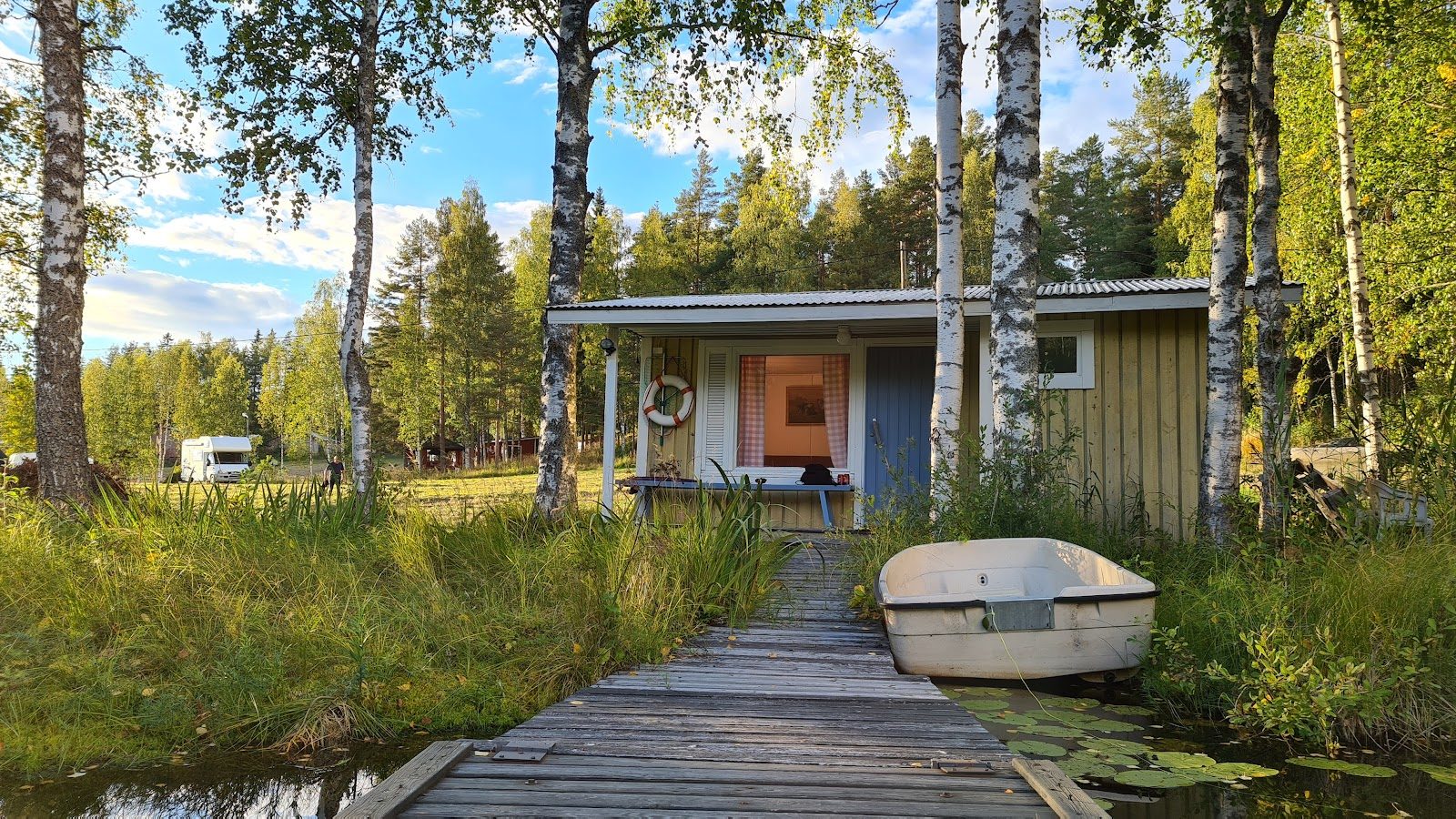 Keltainen aitta järven rannalla, edessä puulaituri ja soutuvene.