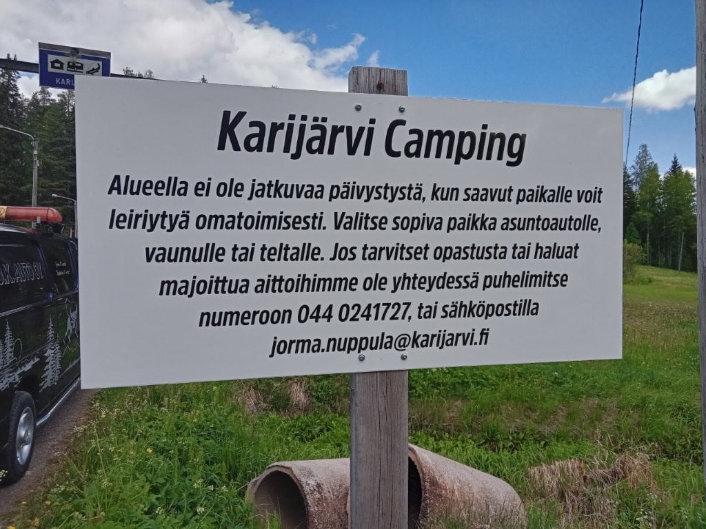 Valkoinen Karijärvi Camping -taulu: alueella ei ole jatkuvaa päivystystä, saapuja voi leiriytyä omatoimisesti ja ottaa yhteyttä puhelimitse tai sähköpostilla.