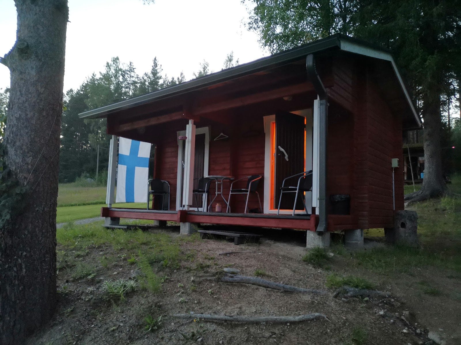 Punainen rantasauna, terassilla tuoleja ja Suomen lippu seinällä.
